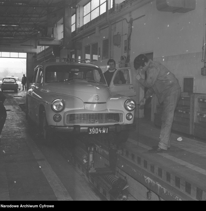 Obiekt Stacja Obsługi Samochodów przy ul. Dzikiej 28. Samochód FSO Warszawa na kanale podczas badania technicznego. Diagnosta mierzy wysokość położenia reflektora, którą przeniesie na ekran. z jednostki Stacje obsługi Stołecznego Przedsiębiorstwa Usług Motoryzacyjnych w Warszawie