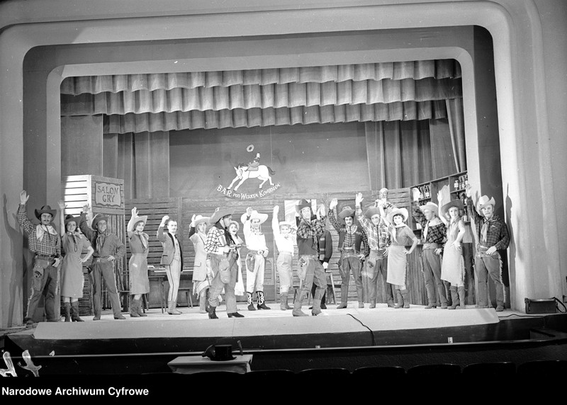 Obiekt Od lewej: NN, Stanisława Górzyńska (tancerka), Andrzej Mirecki (Kowboj II), Danuta Szczepańska (tancerka), Saturnin Żórawski (Horacy), Stefan Witas (Abe Honesty), Kazimierz Brusikiewicz (Grimpo), Barbara Bargiełowska (Winnifred), Wacław Zadroziński (Lemoniadowy Jim), Hanna Bielicka (Tornado Lou), Wacław Jankowski (Dakota Kid), Andrzej Stockinger (Mejico Kid), Jerzy Kamieński (Taper), Stanisław Woliński (Barman), Zofia Karska (tancerka), Jerzy Turek (Kowboj III), Barbara Fandri (Lolo), Leopold Sadurski (Kowboj I). z jednostki Warszawa. Teatr Syrena - sztuka "Jim strzela pierwszy"